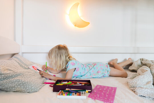 Little girl drawing picture on her bed