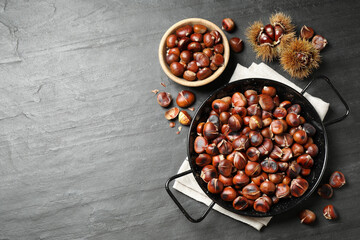 Delicious roasted edible chestnuts on black slate table, flat lay. Space for text