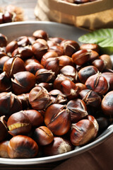 Delicious roasted edible chestnuts in frying pan on table, closeup