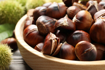 Delicious roasted edible chestnuts in wooden bowl on table, closeup