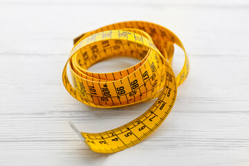 Yellow measuring tape on white wooden table, closeup