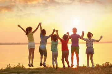 Little children jumping near river at sunset, back view