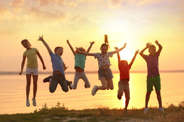 Happy little children jumping near river at sunset