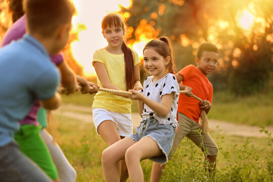 Cute little children playing tug of war game outdoors at sunset