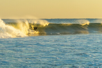 A surfer rides a wave into the sunset.