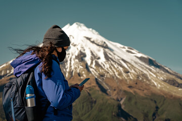 Young woman with face mask looking at her mobil phone while walking in the mountains. Amazing...