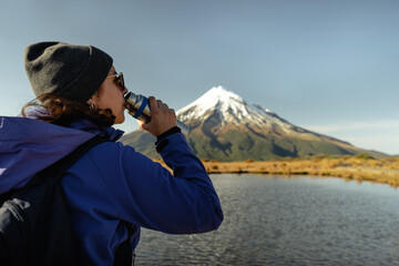 Brunette woman drinking water with the view of Mount Taranaki behind