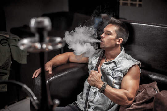 Handsome man blowing clouds of smoke in the hookah bar.