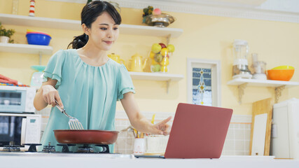 パソコンを見ながら料理する女性　レシピ動画　レシピサイト