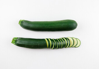 zucchini on a white background.
Two zucchini, one whole and the other sliced, lie in the middle on a white background, top view close-up.