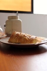 breakfast with a plate with bread in the morning, on a table and with a cup of coffe placed behind it and with natural light coming from the window
