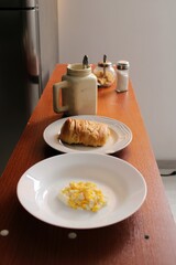 MORNING BREAKFAST WITH COFFEE, A PLATE OF SCRAMBLED EGGS AND A PLATE WITH BREAD ON A COFFEE-COLORED TABLE
