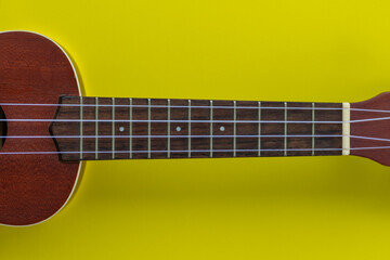 Obraz na płótnie Canvas Closeup top view shot of a wooden ukulele with space for text on a yellow background