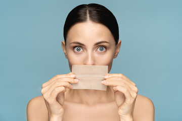 Close up of woman with natural face makeup, holding facial oil blotting paper, hides her lips,...