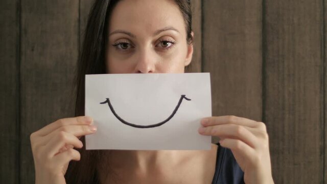 Depressed woman trying to cover problem to smiling painted on paper