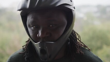 African-American Man Wearing A Black Helmet Looking Directly At The Camera Standing Outdoors - Closeup Shot
