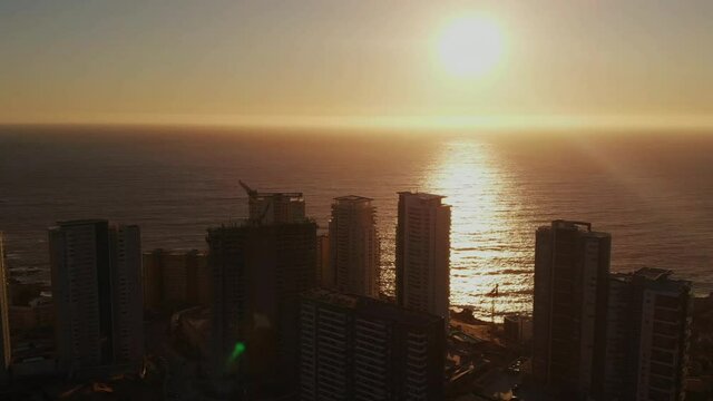 Relaxing vibrant sunset over the ocean and buildings, low angle aerial crane shot