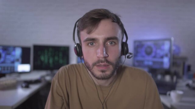 Computer POV of absorbed gamer playing video games. Portrait of young Caucasian man in headphones sitting at night indoors with multiple computers at the background. Programmer coding software.
