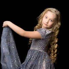 A little girl in a long, elegant dress of a princess on a black background.