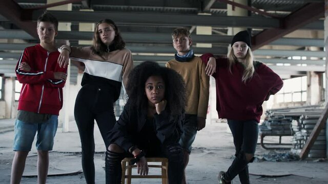 Group of teenagers gang standing indoors in abandoned building, looking at camera.