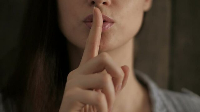 Young woman having secret while holding finger on lips and showing silence sign 