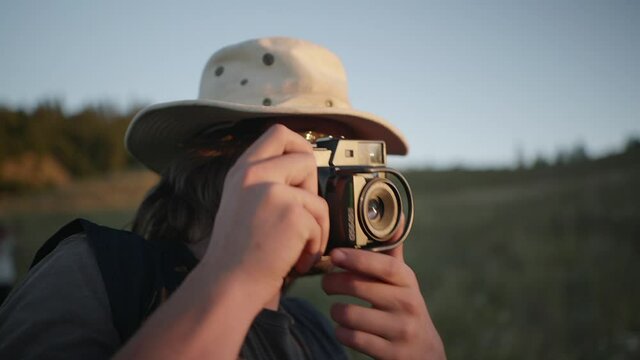 Man with hat and glasses takes nature photos with camera in golden hour