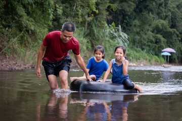 Asian father and his daughters playing in the river together with fun and enjoy with nature.