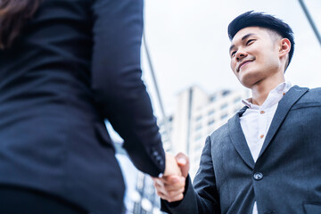 Asian business people making handshake with skyscraper background.