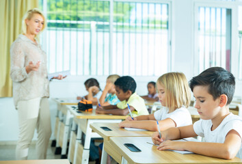 Fototapeta premium Side view of schoolkids group working on lecture in classroom, making notes