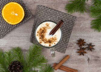 Traditional holiday drink eggnog. sweet drink based on raw chicken eggs and milk. Christmas cocktail with grated nutmeg and cinnamon. background of a spruce branch with cones. top view, copy space.