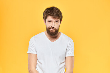 Fototapeta premium Bearded man in a white T-shirt gestures with his hands emotions studio yellow background