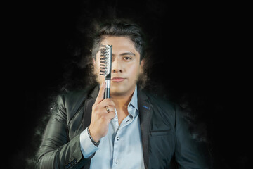 Hispanic man covering his eye with a hair comb in front of a black background