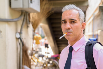 Face of Persian businessman with gray hair smoking cigarette in the city streets