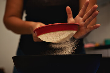 hands of a woman straining flour for a cake