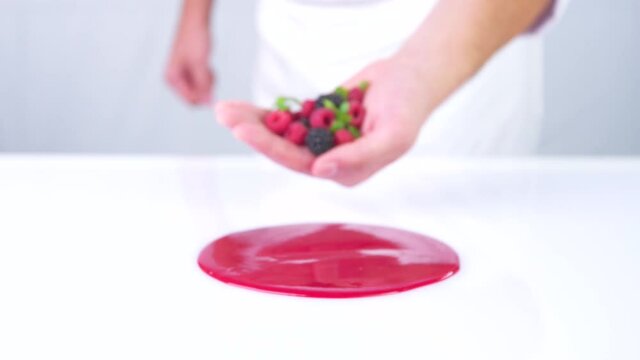 The berries are falling from the hand to the red sauce. The pastry chef is decorating the dessert. Making a beautiful dessert macro slow motion.