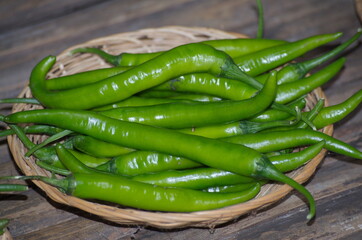 Green peppers in the wicker basket on wooden background.