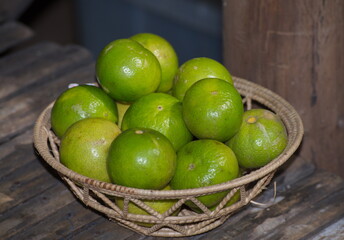 Green lemon in the wicker basket on wooden background.