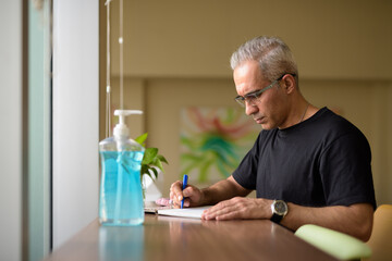 Handsome Persian man with gray hair writing at the library