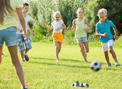 Active Kids Having Fun And Kicking Football In Park On Summer Day