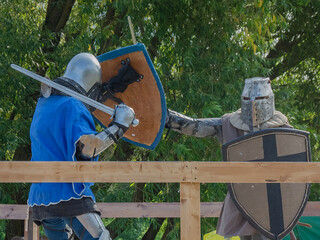Two foot warriors in heavy medieval armor fight in the arena. Armed with swords. They are protected...