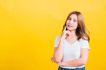 Portrait Asian Thai beautiful young woman wearing white t-shirt standing chin handle relaxed thinking about something about the question studio shot, isolated on yellow background with copy space