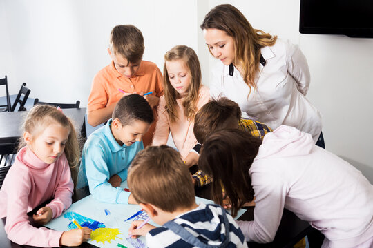 Team of elementary age children and beutiful teacher drawing on one sheet