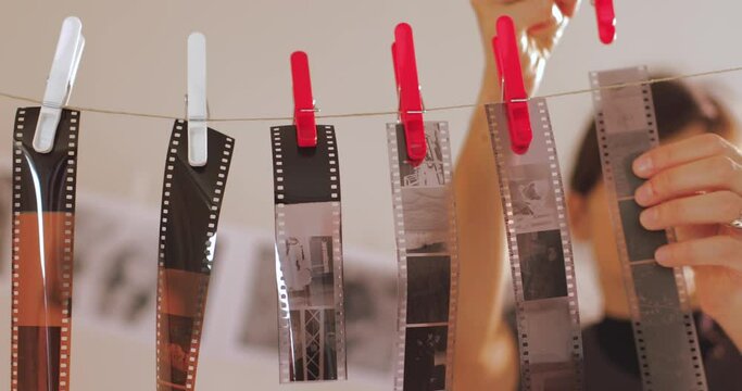 Female photographer hanging filmstrip negatives after developing it in darkroom. Portrait of creative girl photographer in photo studio darkroom. Developing analog camera film.