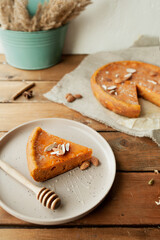 cozy home-made autumn vegan dinner, pumpkin pie with almonds, honey stick and whole pie on rough canvas napkin on wooden table with bouquet of dried flowers in the background, selective focus