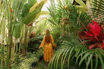 Back view girl in yellow dress walking through tropical garden