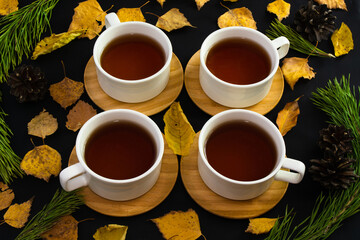 Four tea cups on black background with pine branches and pine cones, autumn leaves. Tea in company concept