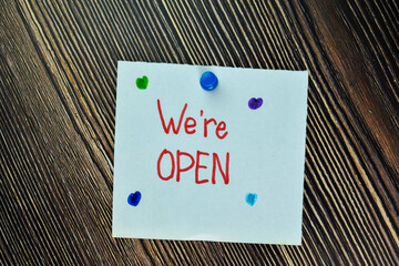 We're Open write on sticky note and isolated on Wooden Table. Business Concept