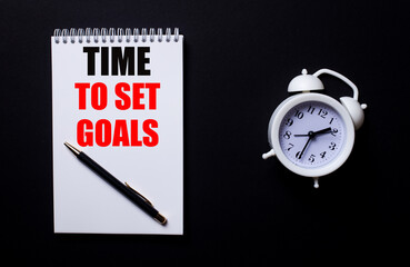 TIME TO SET GOALS is written in a white notepad near a white alarm clock on a black background.