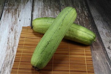 Pile of fresh and organic green sponge gourd fruit on the wooden mat. Famous tropical vegetable ingredient in Asia restaurant. High fiber and vitamin. 