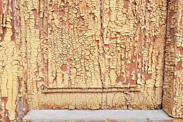 Texture of old wooden door of abandoned building with peeled yellow paint abstract background.